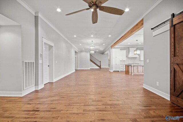 unfurnished living room with a barn door, light hardwood / wood-style floors, ceiling fan with notable chandelier, and ornamental molding