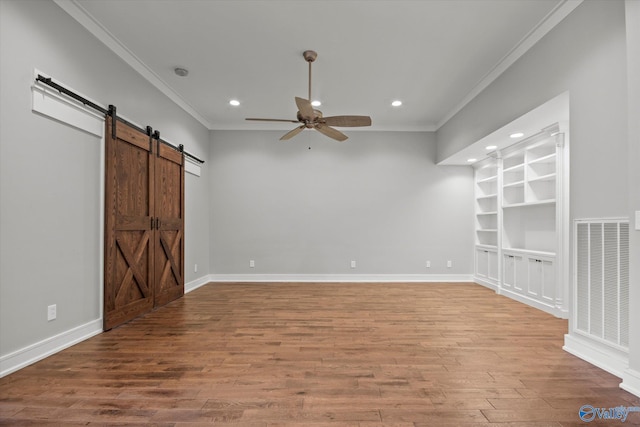 spare room featuring hardwood / wood-style floors, a barn door, built in features, and ornamental molding