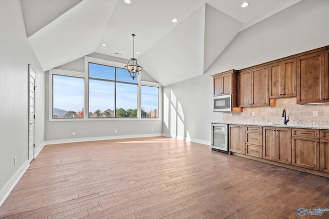 kitchen featuring sink, wine cooler, decorative backsplash, light stone countertops, and decorative light fixtures