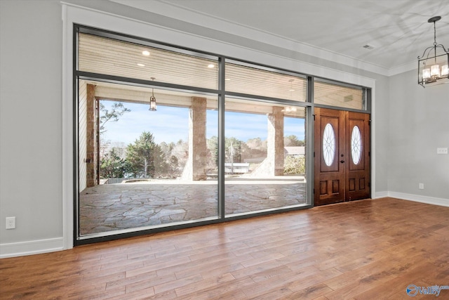 foyer featuring wood-type flooring, crown molding, and an inviting chandelier