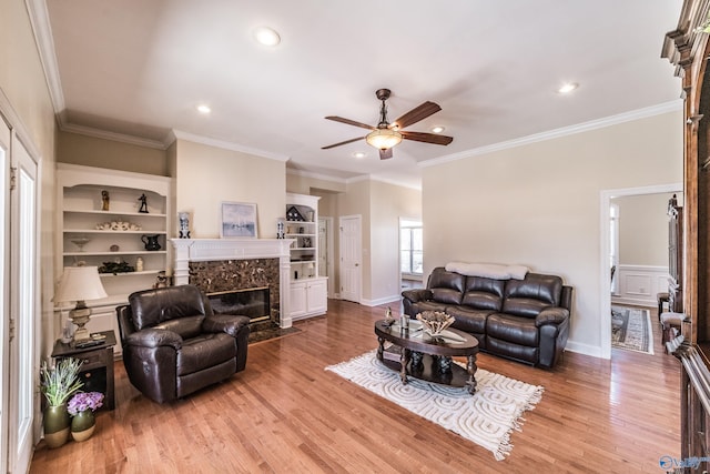 living area with a ceiling fan, wood finished floors, crown molding, a premium fireplace, and baseboards