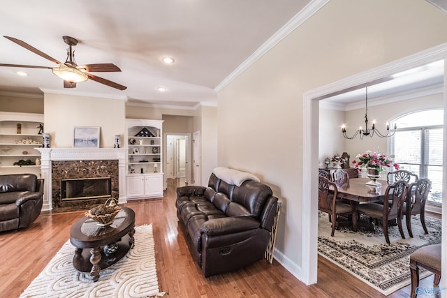 living room with wood finished floors, baseboards, a high end fireplace, crown molding, and ceiling fan with notable chandelier