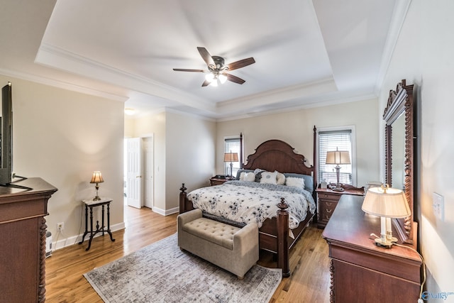 bedroom featuring light wood-type flooring, a tray ceiling, and baseboards