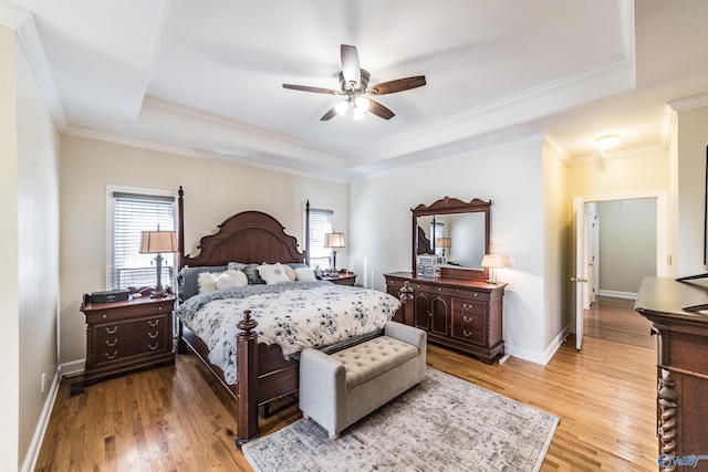 bedroom featuring baseboards, multiple windows, a raised ceiling, and light wood finished floors