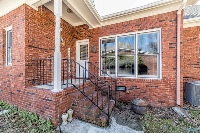 view of exterior entry with brick siding, crawl space, and central AC unit