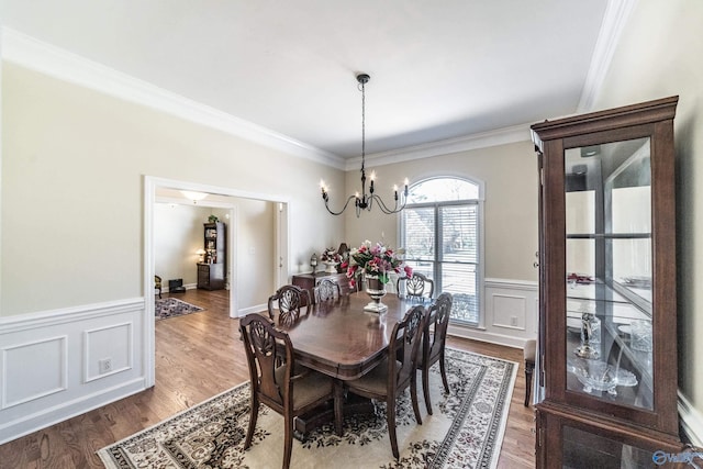 dining room featuring crown molding, a chandelier, a wainscoted wall, wood finished floors, and a decorative wall