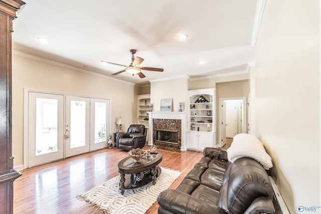 living area featuring built in features, light wood finished floors, a fireplace, ceiling fan, and ornamental molding