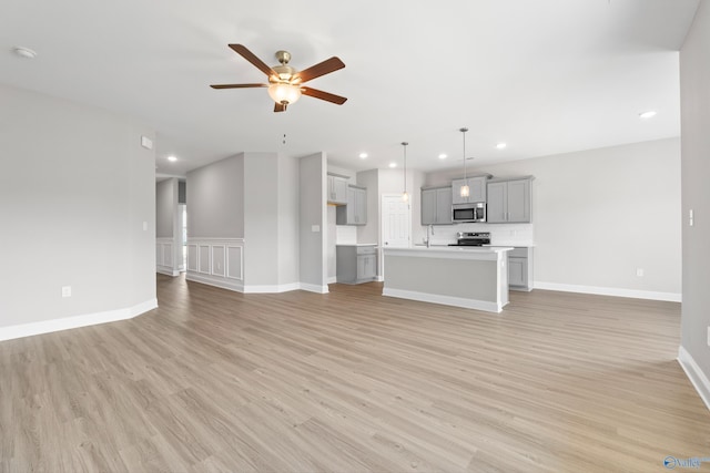 unfurnished living room with baseboards, ceiling fan, recessed lighting, light wood-style floors, and a sink