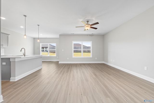 unfurnished living room with light wood-style flooring, a sink, recessed lighting, baseboards, and ceiling fan