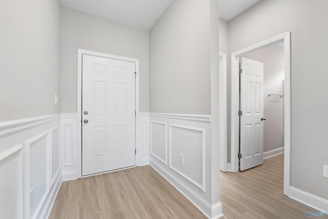 entryway with light wood-type flooring, a wainscoted wall, and a decorative wall