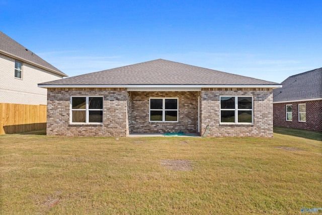 rear view of property with brick siding, fence, a lawn, and roof with shingles