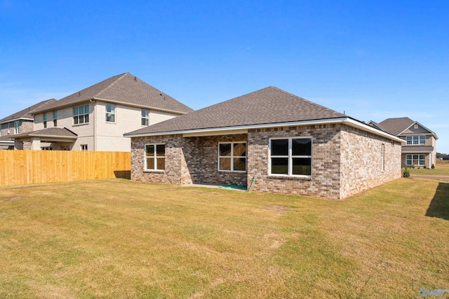 rear view of house featuring brick siding, fence, and a lawn