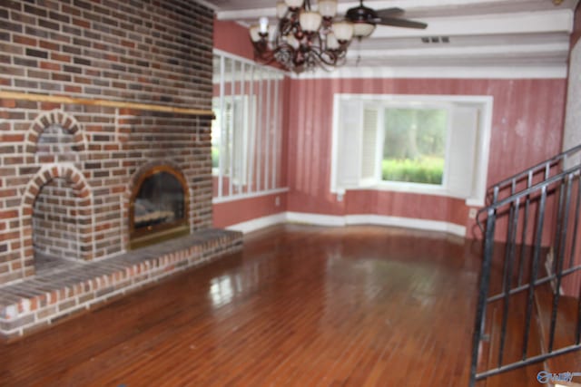 unfurnished living room with a notable chandelier, a brick fireplace, and hardwood / wood-style flooring