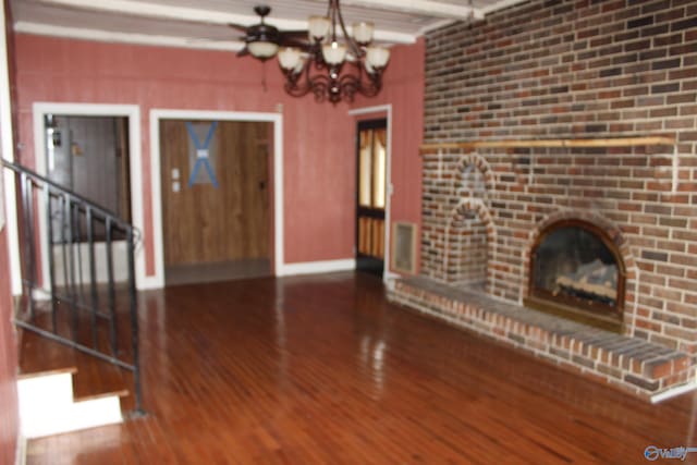 unfurnished living room featuring a brick fireplace, a notable chandelier, beam ceiling, and hardwood / wood-style floors