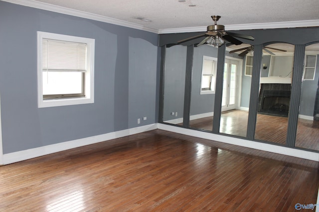 empty room featuring a textured ceiling, wood-type flooring, crown molding, and a wealth of natural light