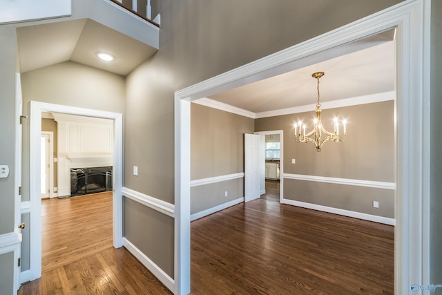 interior space featuring crown molding, lofted ceiling, dark wood-type flooring, and an inviting chandelier