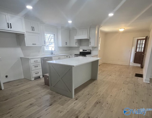 kitchen with stainless steel appliances, sink, custom range hood, a center island, and white cabinets