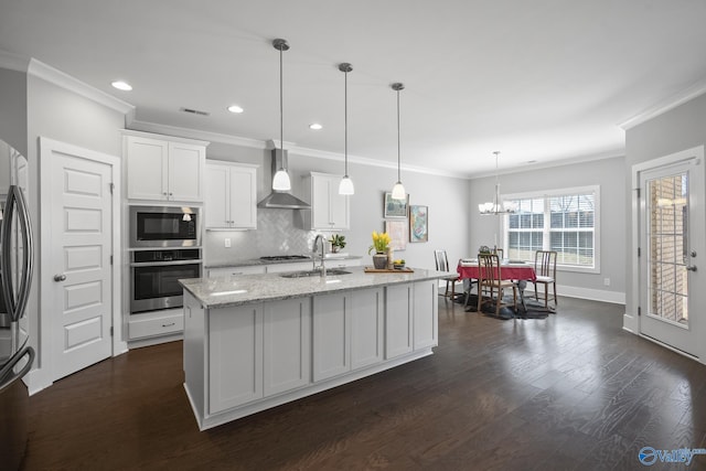 kitchen featuring appliances with stainless steel finishes, dark wood-style floors, white cabinets, wall chimney exhaust hood, and a sink