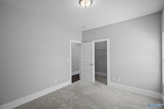 unfurnished bedroom with a spacious closet, carpet flooring, baseboards, and a closet