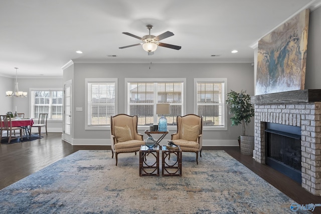 sitting room featuring a brick fireplace, baseboards, ornamental molding, ceiling fan with notable chandelier, and wood finished floors