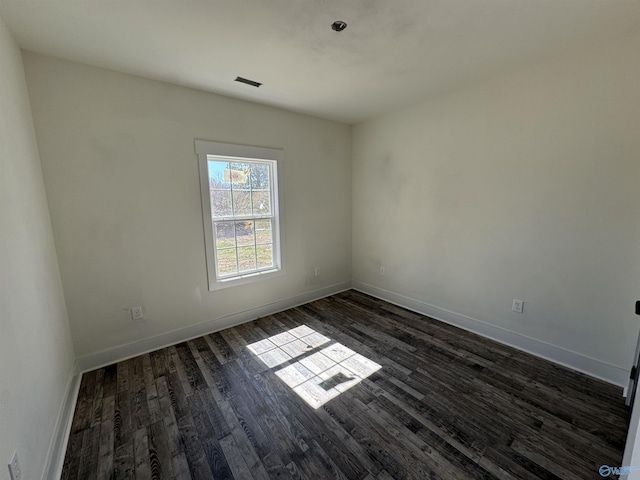 spare room with visible vents, baseboards, and dark wood-type flooring