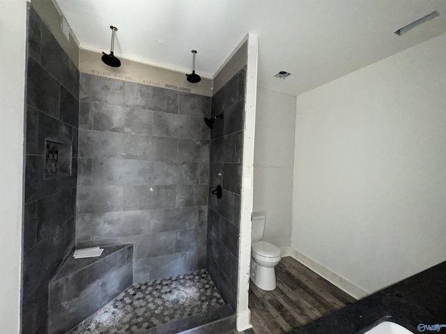 full bath featuring a tile shower, wood finished floors, toilet, and baseboards