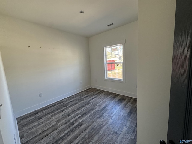 spare room with baseboards, visible vents, and dark wood-style flooring