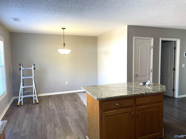 kitchen featuring dark wood-style flooring, visible vents, baseboards, hanging light fixtures, and a center island