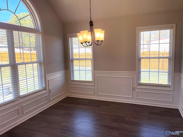 unfurnished dining area with lofted ceiling, a wainscoted wall, a notable chandelier, and dark wood-style flooring