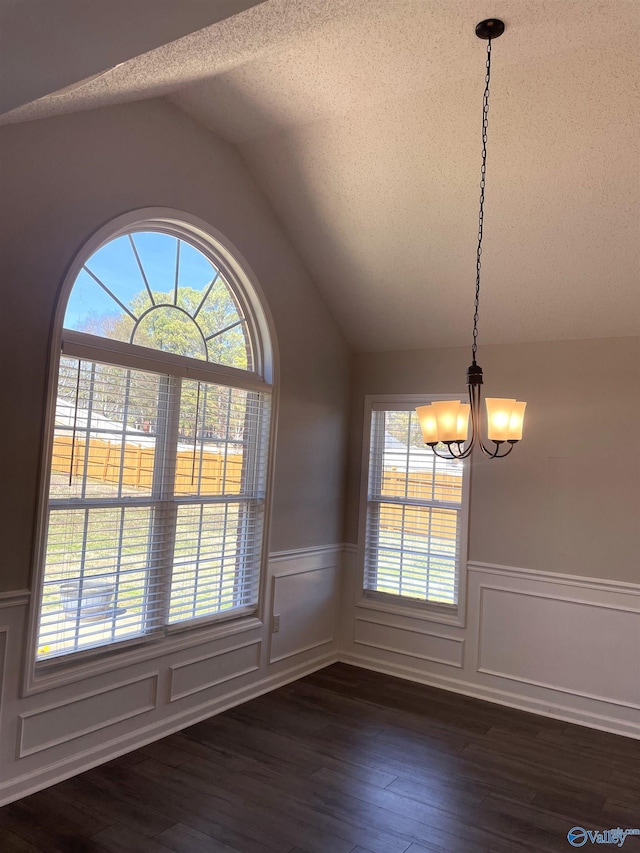 unfurnished dining area with a wainscoted wall, dark wood-style flooring, an inviting chandelier, vaulted ceiling, and a textured ceiling