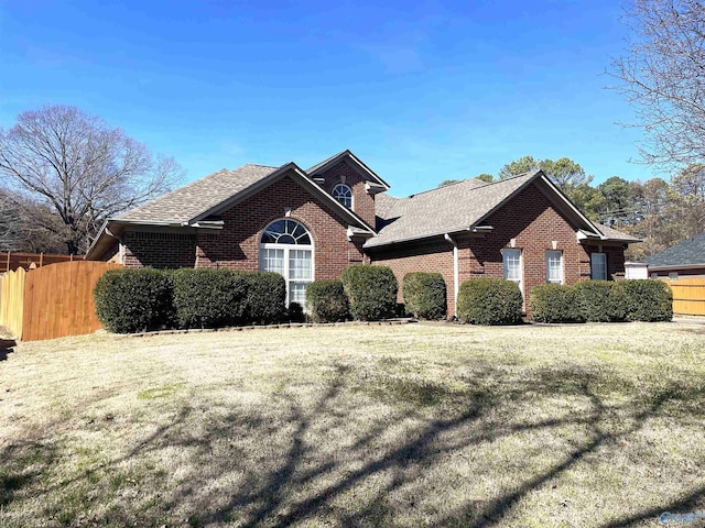 view of front facade featuring brick siding, a front lawn, a shingled roof, and fence