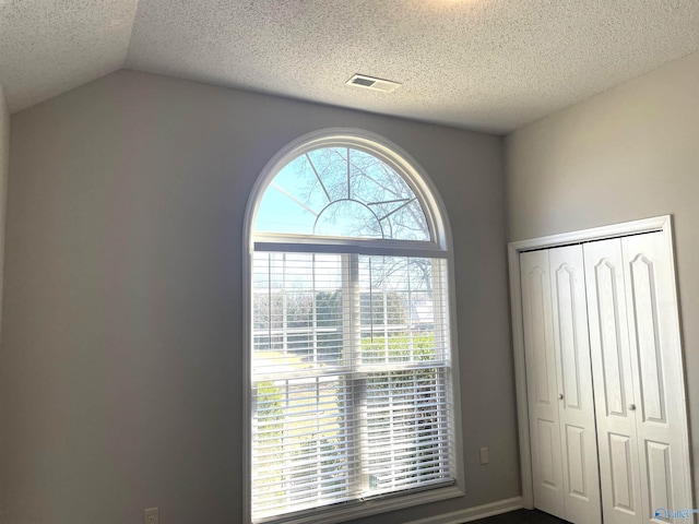 unfurnished bedroom featuring vaulted ceiling, a textured ceiling, a closet, and visible vents