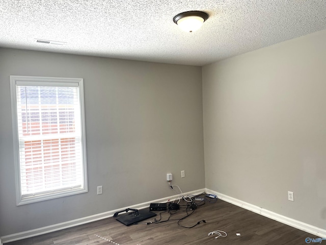 unfurnished room featuring dark wood-style floors, baseboards, visible vents, and a textured ceiling