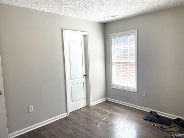 unfurnished bedroom with a textured ceiling, dark wood-style flooring, and baseboards