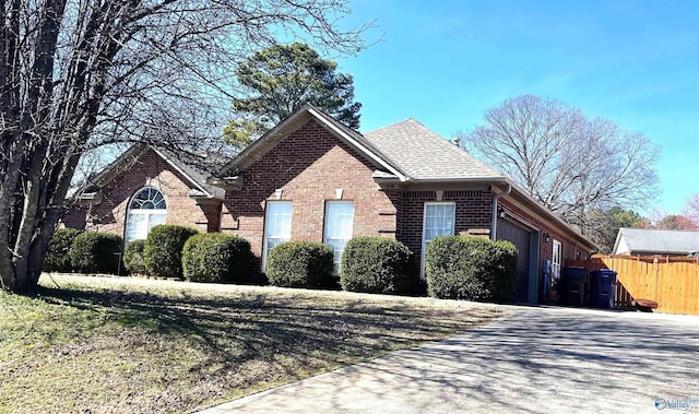 view of front of property featuring a garage, brick siding, driveway, and fence