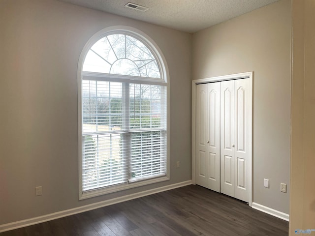 unfurnished bedroom with a textured ceiling, visible vents, baseboards, a closet, and dark wood finished floors