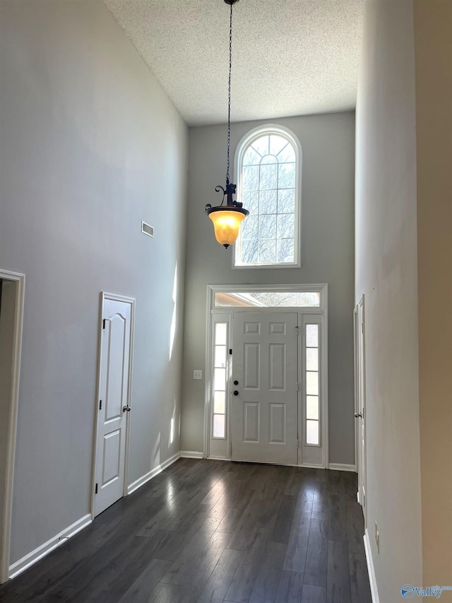 foyer entrance with dark wood-type flooring, baseboards, visible vents, and a high ceiling