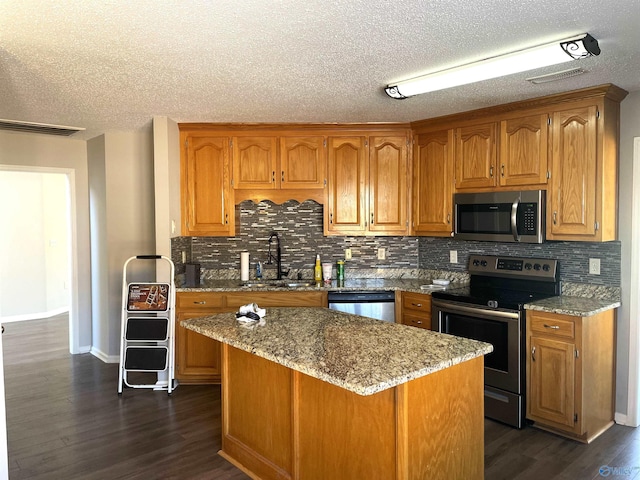 kitchen featuring appliances with stainless steel finishes, light stone countertops, a sink, and dark wood-style floors