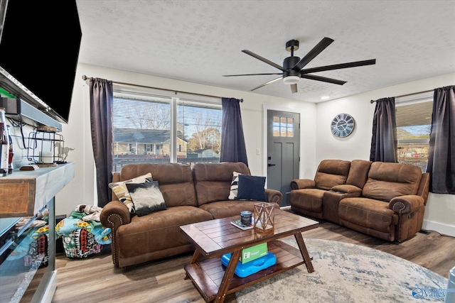 living area with ceiling fan, a textured ceiling, baseboards, and wood finished floors