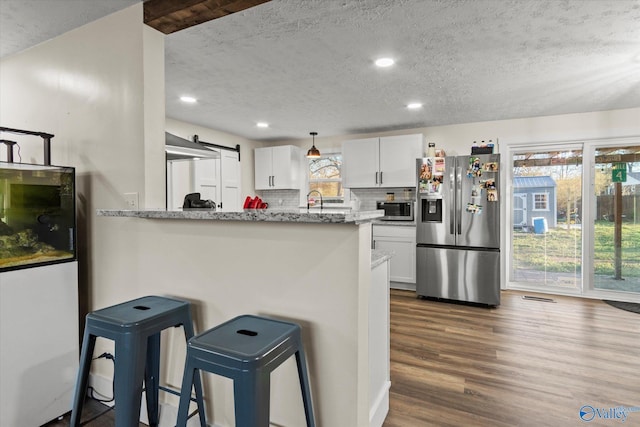 kitchen with white cabinets, dark wood finished floors, decorative backsplash, a breakfast bar area, and stainless steel appliances