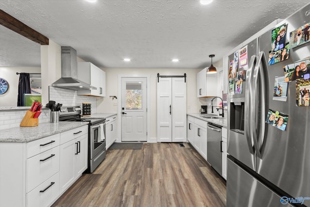 kitchen featuring dark wood-style floors, stainless steel appliances, tasteful backsplash, a barn door, and wall chimney exhaust hood