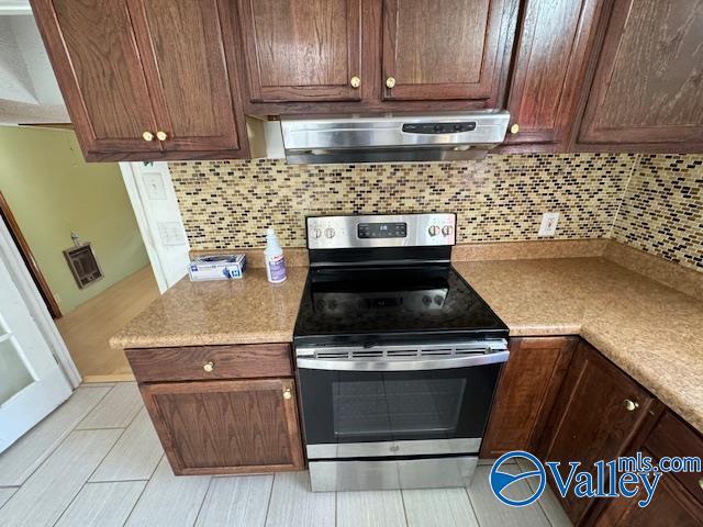 kitchen with stainless steel electric range, light tile patterned floors, backsplash, and exhaust hood