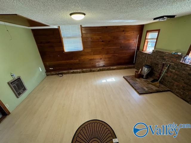 unfurnished living room with light hardwood / wood-style floors, heating unit, and wood walls