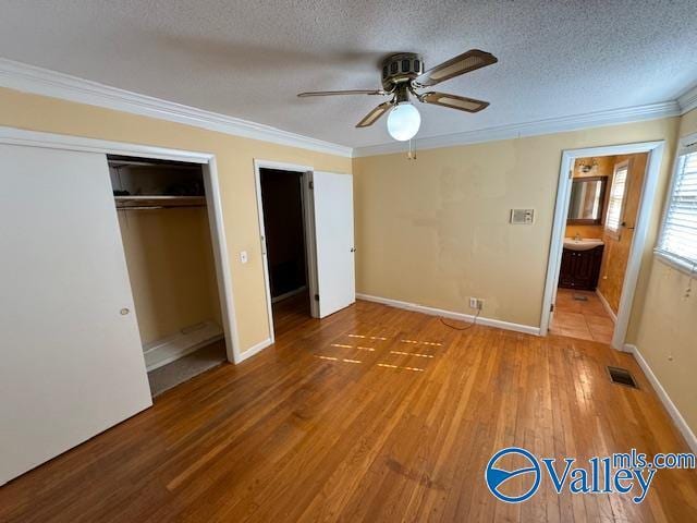 unfurnished bedroom featuring ensuite bathroom, hardwood / wood-style flooring, ceiling fan, a textured ceiling, and a closet