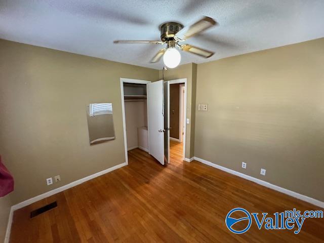 unfurnished bedroom with hardwood / wood-style floors, a textured ceiling, a closet, and ceiling fan