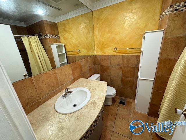 bathroom featuring tile patterned flooring, toilet, tile walls, and crown molding