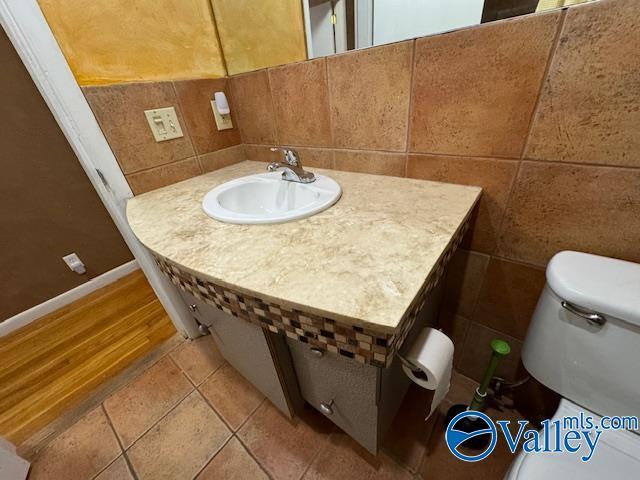 bathroom with tile patterned floors, toilet, sink, and tile walls