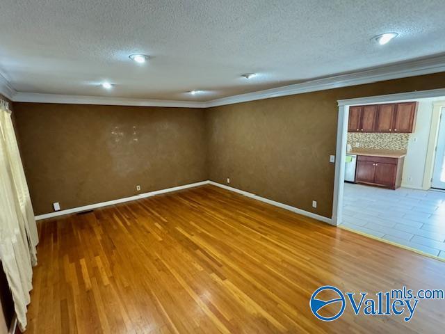 unfurnished room featuring a textured ceiling, light hardwood / wood-style floors, and ornamental molding