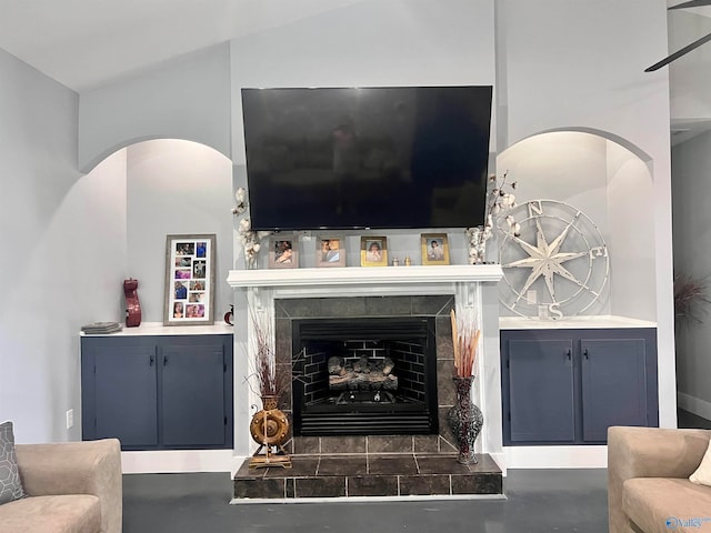 living room with ceiling fan, a tiled fireplace, and vaulted ceiling