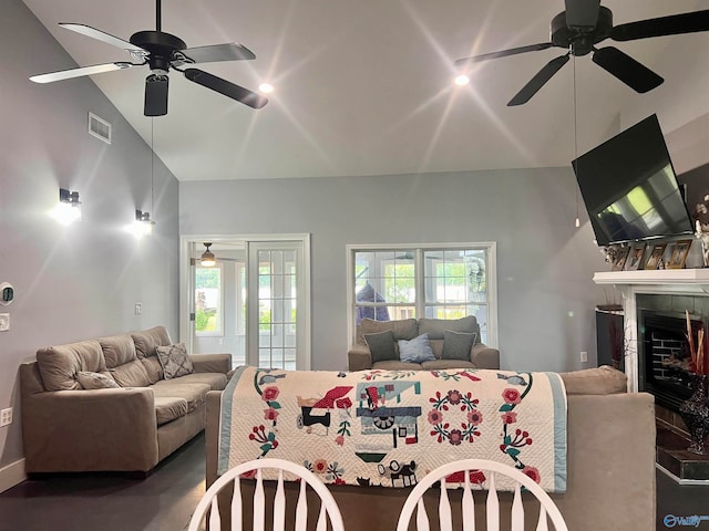 living room with ceiling fan, vaulted ceiling, and a tile fireplace